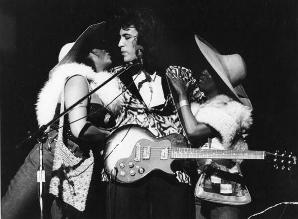 Bill Spooner at the microphone flanked by two women in cowboy hats and fur vests, black-and-white early Tubes live shot