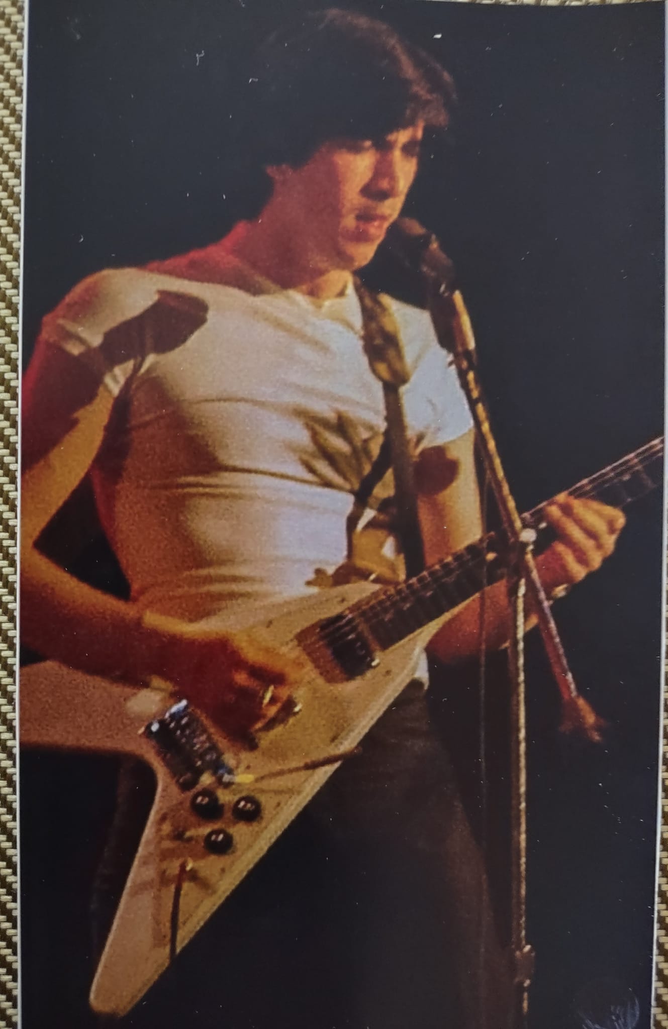 Bill Spooner in a white t-shirt playing his white Flying V guitar at the microphone — early Tubes color live shot