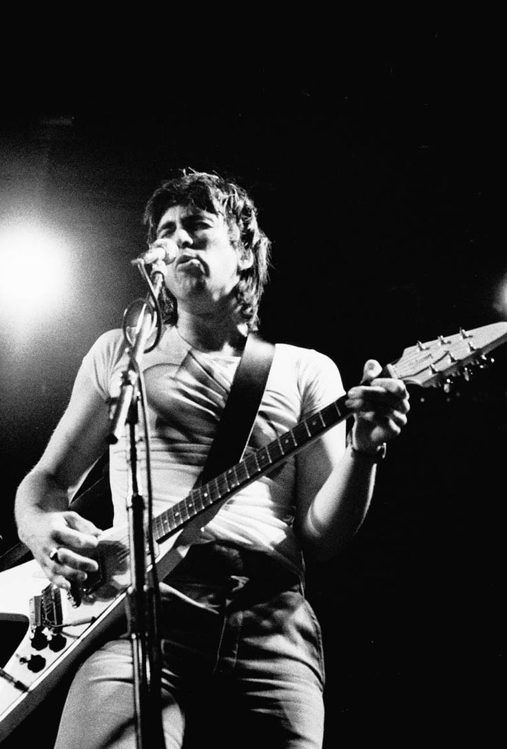 Bill Spooner singing at the microphone while playing his Flying V guitar, black-and-white close-up