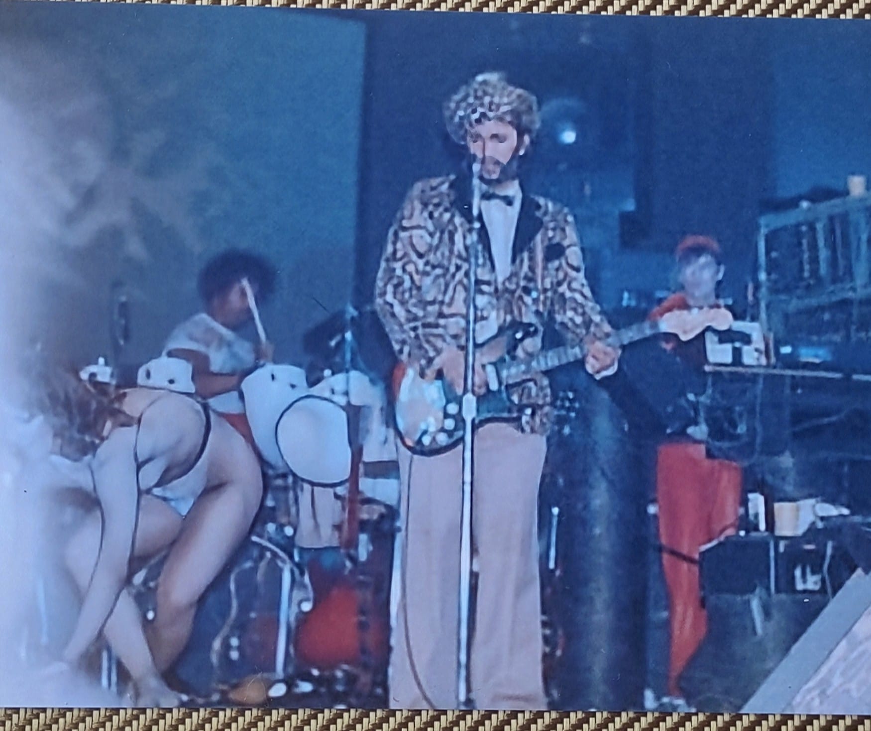 Bill Spooner on stage in a leopard print jacket and bow tie playing guitar — Tubes theatrical performance with dancer in foreground