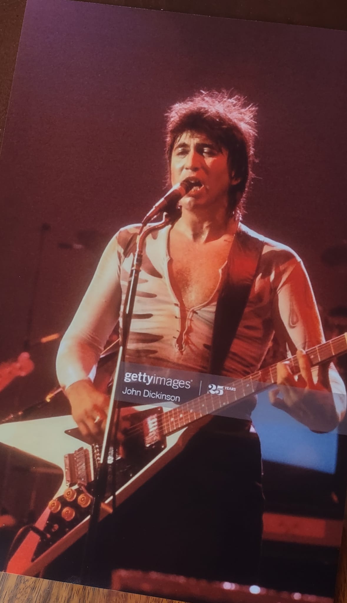Bill Spooner at the microphone playing Flying V under red stage lights, open shirt — color live shot, photo: John Dickinson / Getty