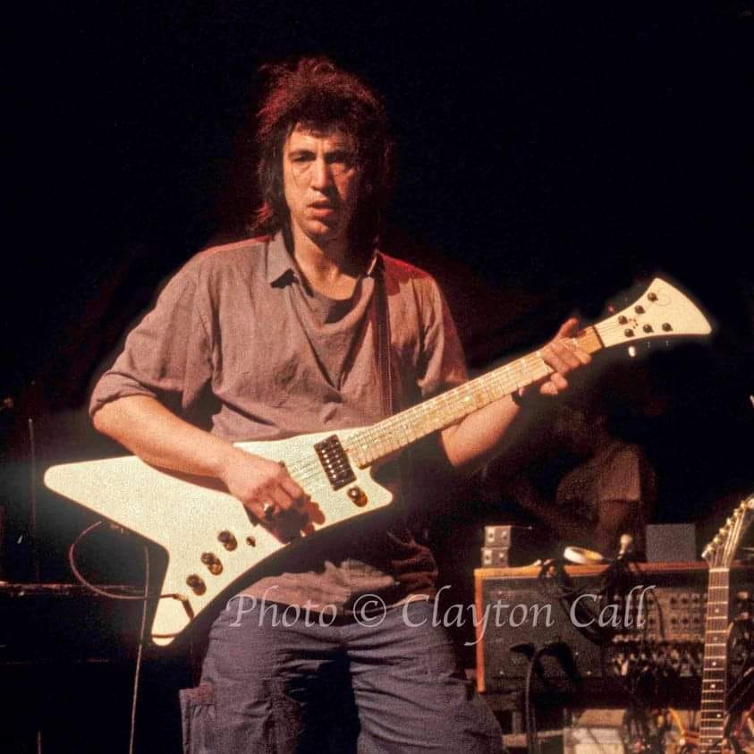 Bill Spooner on stage holding his white Flying V guitar — color portrait, photo by Clayton Call