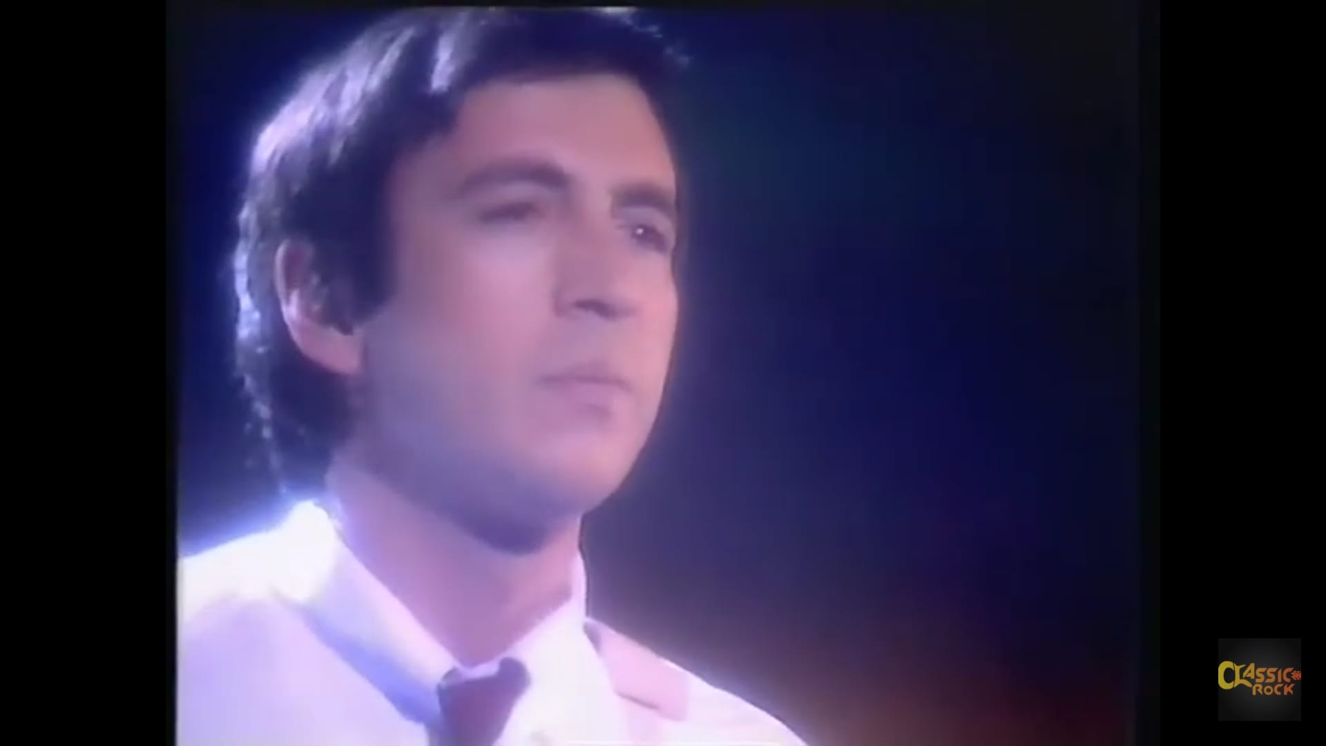 Bill Spooner close-up — face in dramatic light with white shirt and tie, TV broadcast still