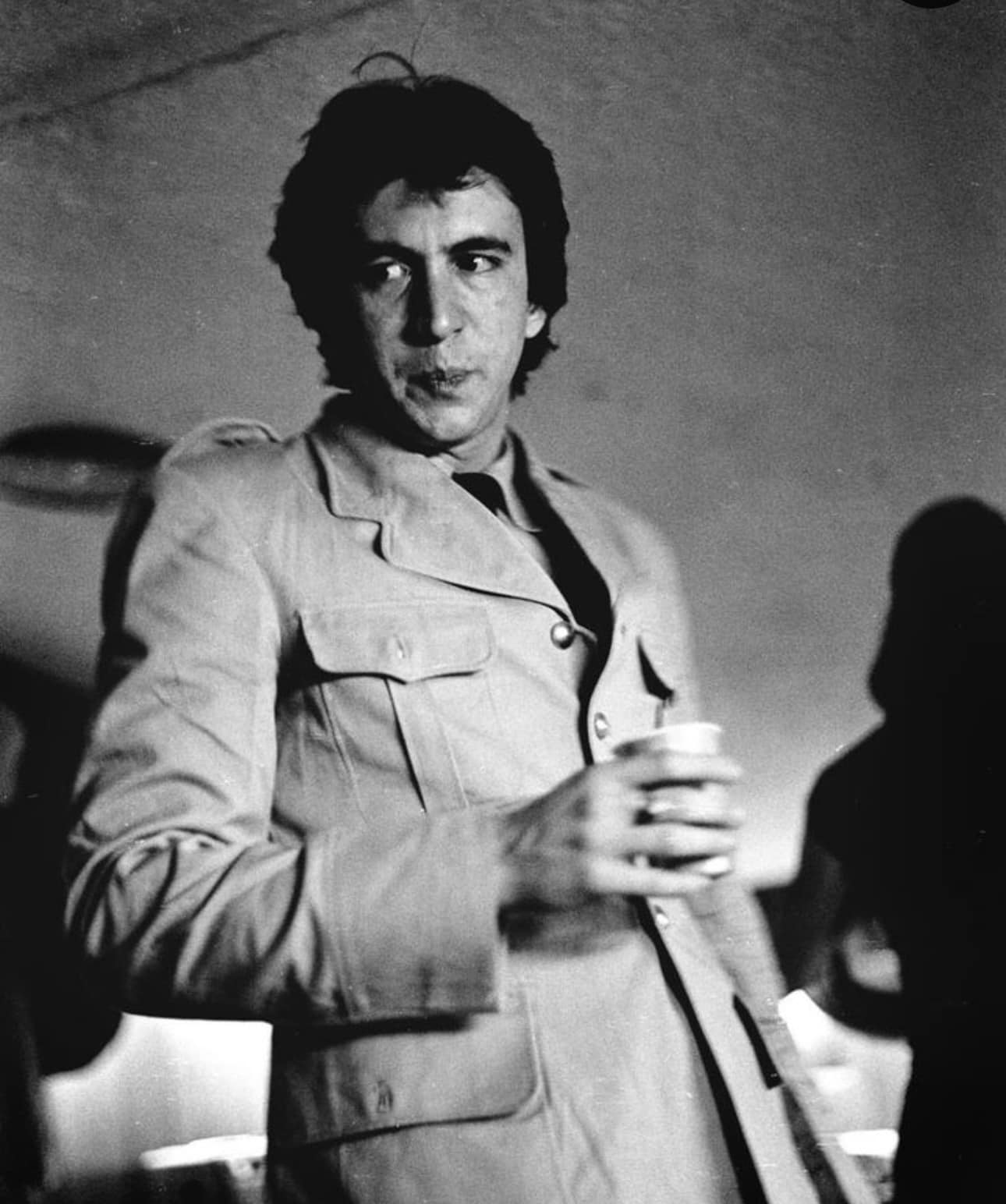 Bill Spooner backstage in a military-style jacket holding a drink — black-and-white candid portrait