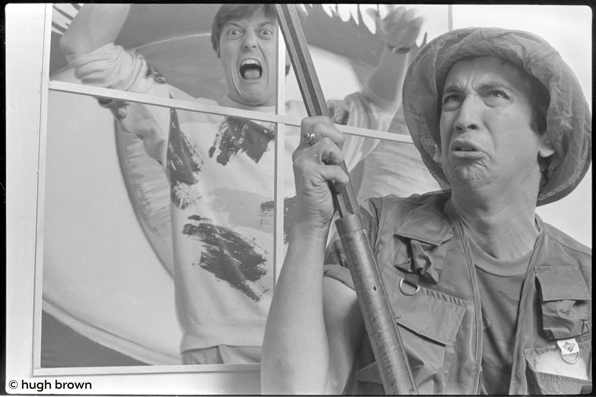 Bill Spooner in a military safari hat holding a prop rifle, another performer screaming through a window frame — dramatic black-and-white, photo: Hugh Brown