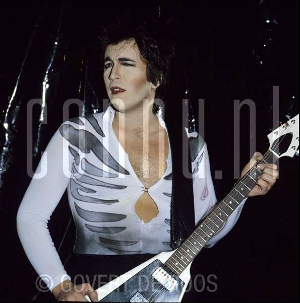 Bill Spooner on stage in a white skeleton-print shirt with his white Flying V guitar, 1977