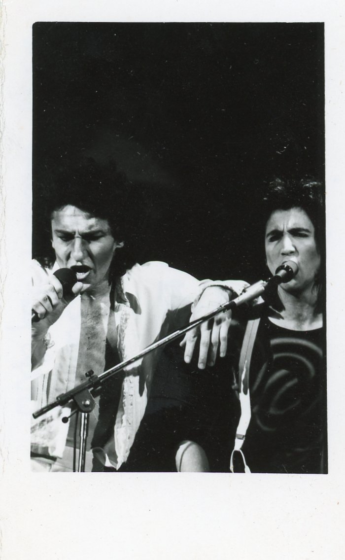 Bill Spooner and Fee Waybill sharing microphones on stage, intense black-and-white shot