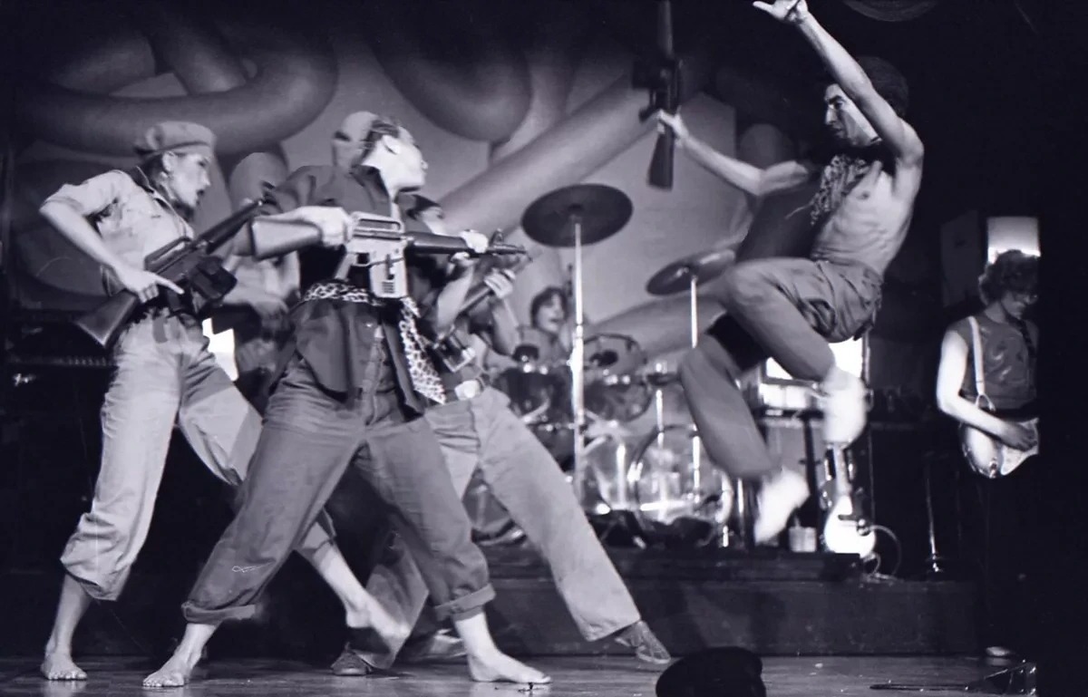 The Tubes 'Attack of the Fifty Foot Woman'-style stage routine — dancers with prop assault rifles as Fee Waybill leaps mid-air