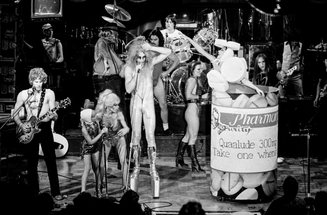 The Tubes performing 'White Punks on Dope' — Quay Lewd center stage in platform boots next to a giant Quaalude 300mg prop bottle, dancers flanking the stage