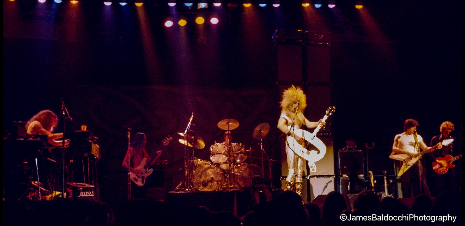 The Tubes on a large theater stage — Quay Lewd in giant platform boots center, full band arrayed under purple and pink lights (photo: James Baldocchi)