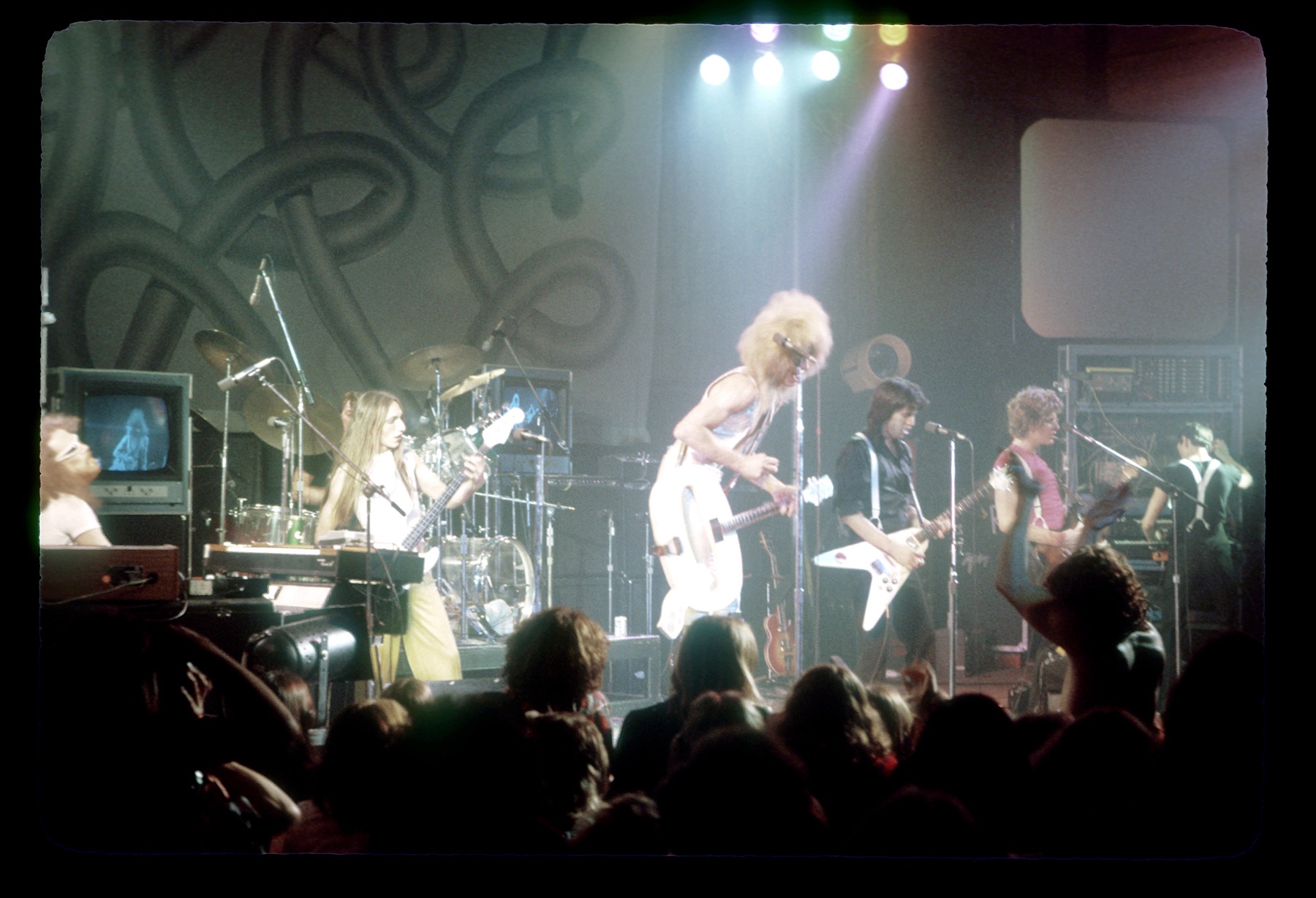The Tubes live in color — full band on stage with Bill Spooner and Roger Steen on Flying V guitars, Prairie Prince on drums behind